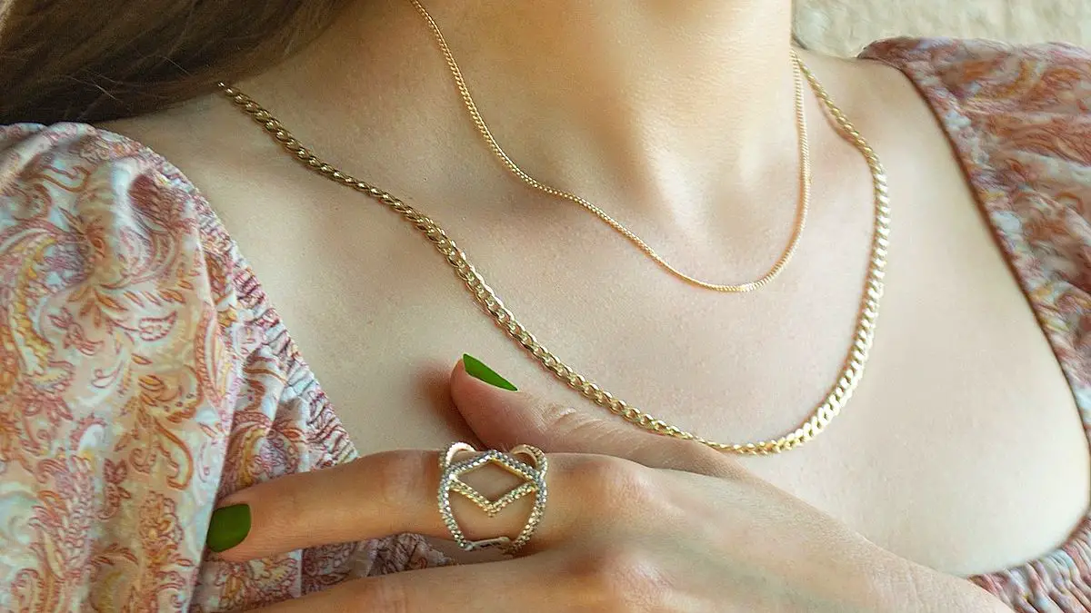 A woman wearing two metal necklaces and one metal ring. She is also wearing green nail polish.