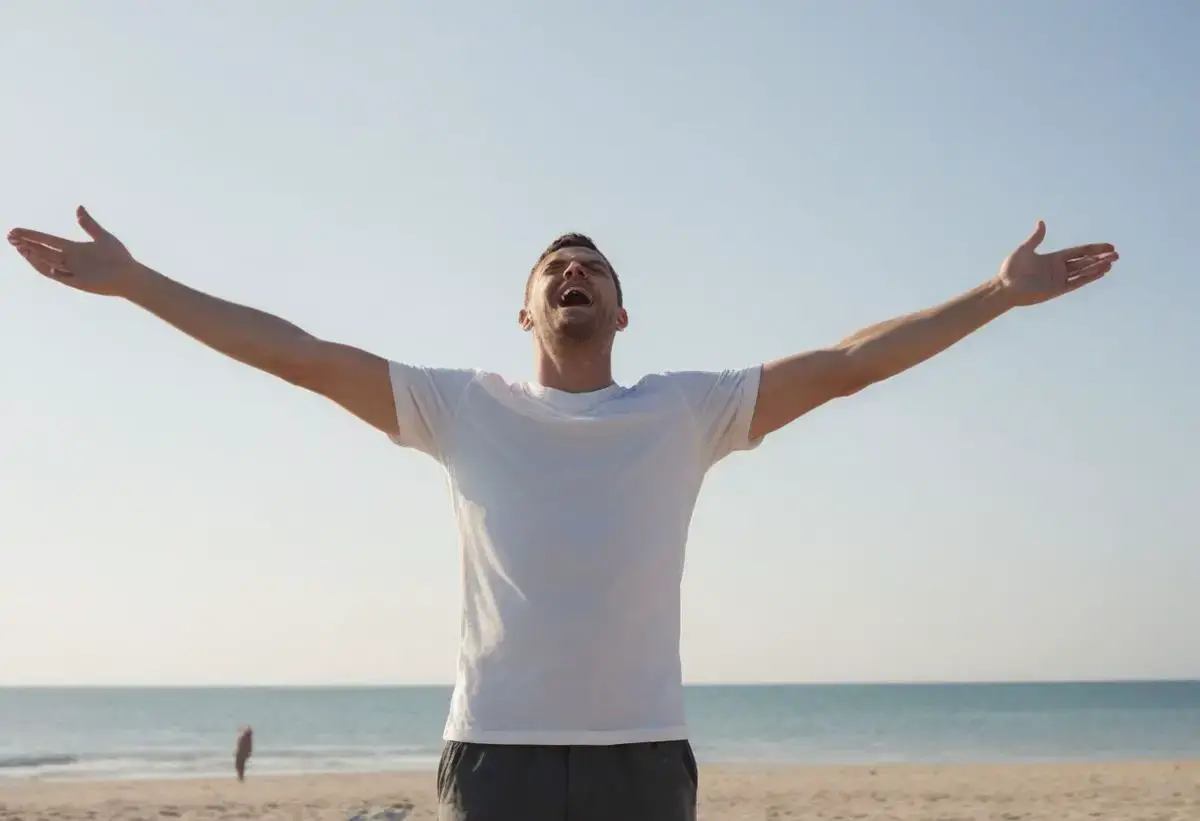 A happy man with his arms in the air with joy while at the beach.