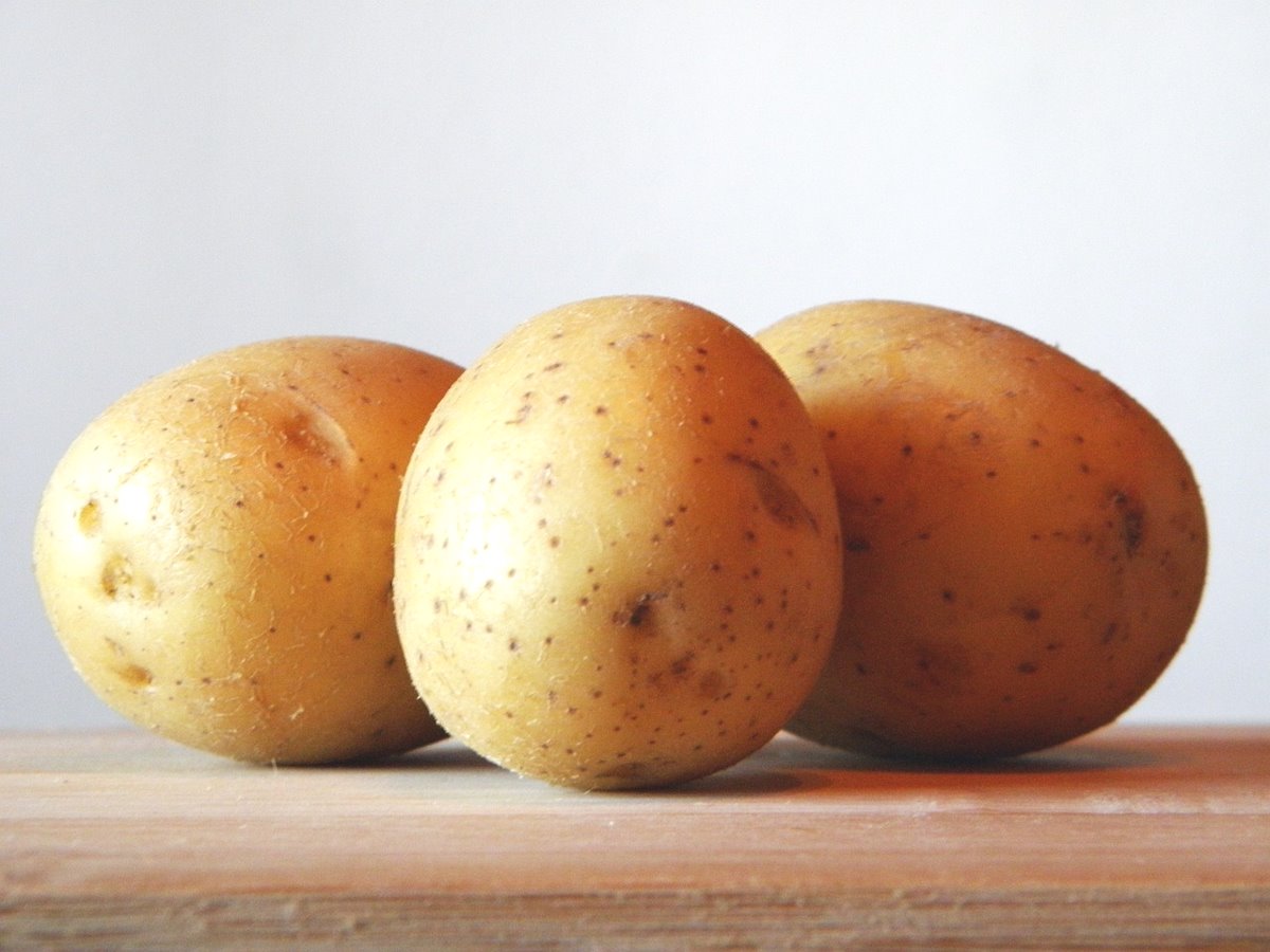 Three potatoes sitting on a wooden table top with a white background.