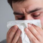 Man sneezing into a tissue. Sneezing was caused by a cold or allergies.